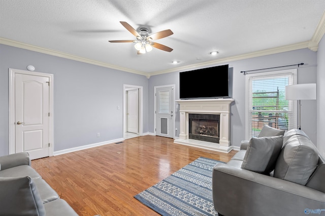 living area featuring ornamental molding, a ceiling fan, light wood-style flooring, and a fireplace with raised hearth