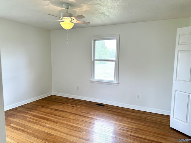 spare room with a textured ceiling, light wood-style flooring, visible vents, baseboards, and a ceiling fan