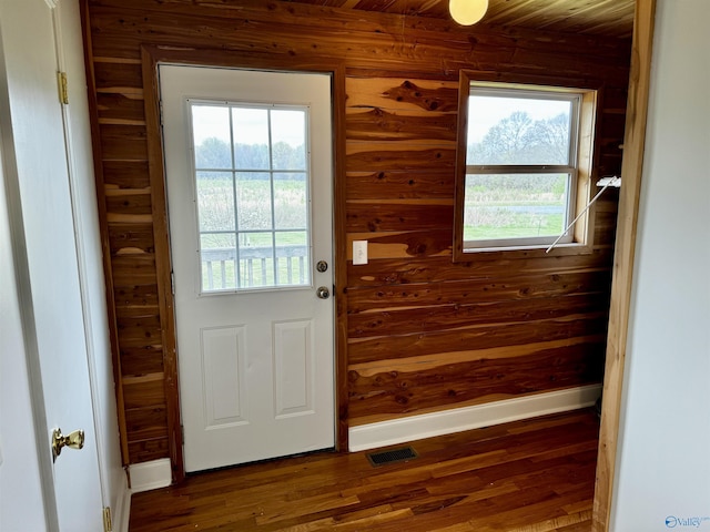 entryway with a wealth of natural light, wooden walls, dark wood-style flooring, and baseboards