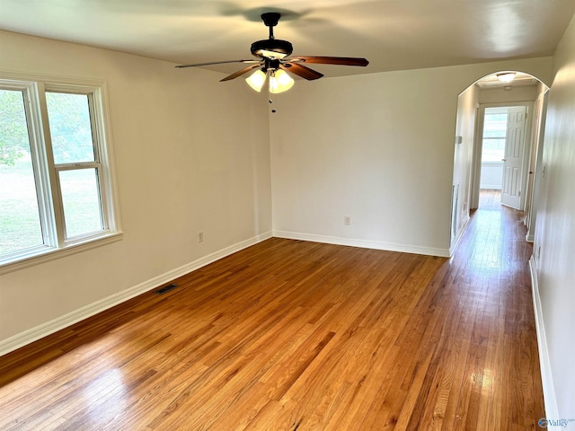 spare room with plenty of natural light, light wood-type flooring, a ceiling fan, and arched walkways