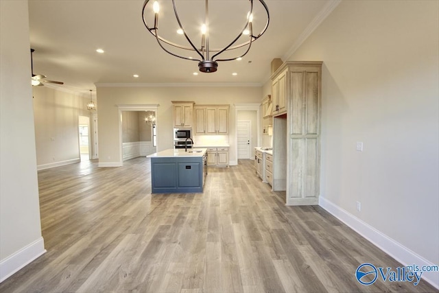 kitchen featuring built in microwave, sink, an island with sink, ceiling fan with notable chandelier, and ornamental molding