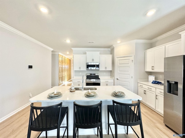 kitchen featuring stainless steel appliances, a sink, ornamental molding, a breakfast bar area, and white cabinetry