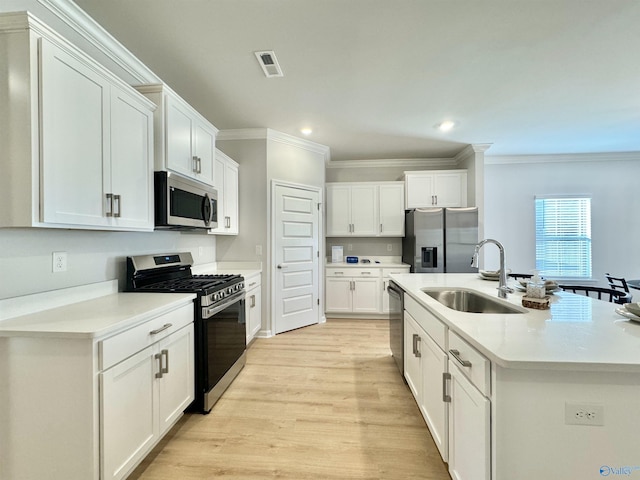 kitchen featuring stainless steel appliances, a sink, crown molding, white cabinetry, and light wood-type flooring