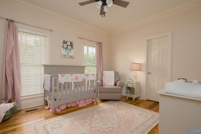 bedroom with light wood-type flooring, crown molding, a nursery area, and ceiling fan