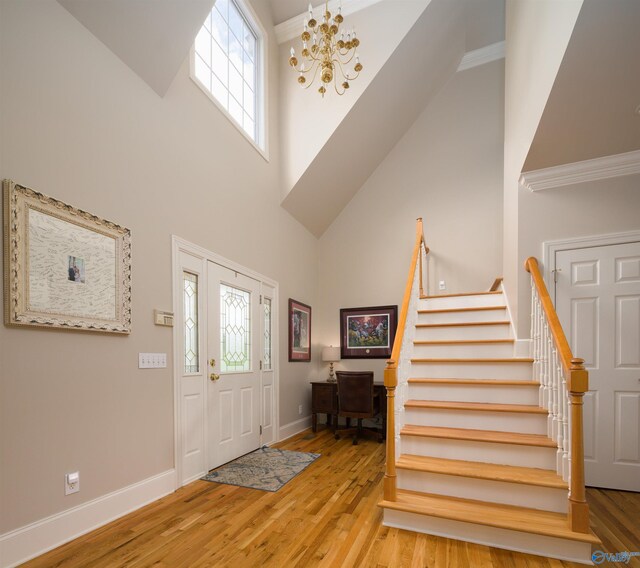 foyer entrance featuring a notable chandelier, ornamental molding, light wood-type flooring, and a towering ceiling