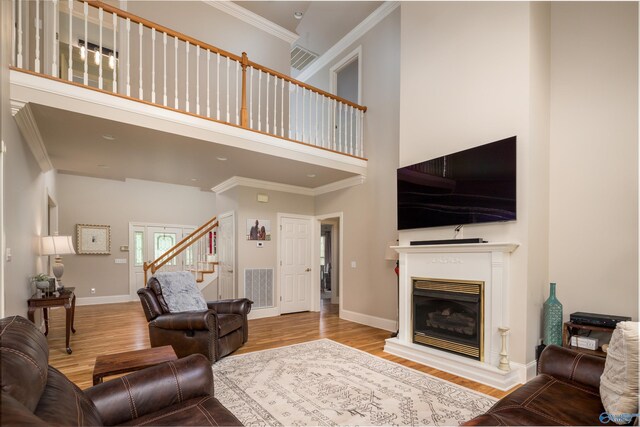 living room featuring crown molding, light wood-type flooring, and a high ceiling