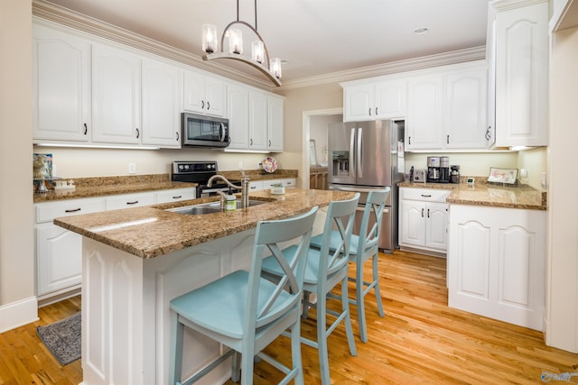 kitchen featuring a breakfast bar, light wood-type flooring, stainless steel appliances, pendant lighting, and a center island with sink