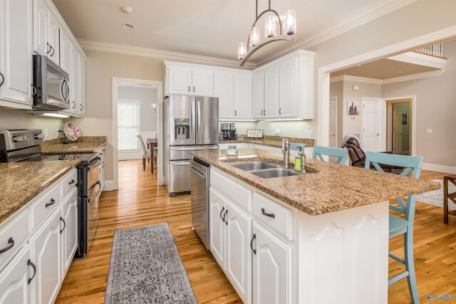 kitchen featuring an island with sink, stainless steel appliances, light hardwood / wood-style floors, decorative light fixtures, and sink