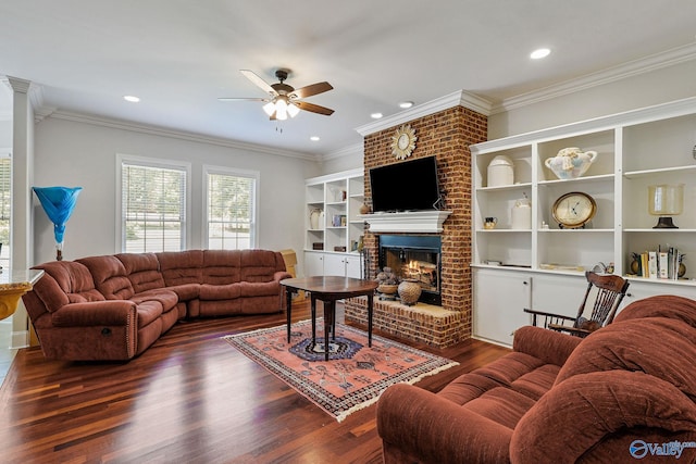 living room featuring dark wood-type flooring, ceiling fan, ornamental molding, and a brick fireplace