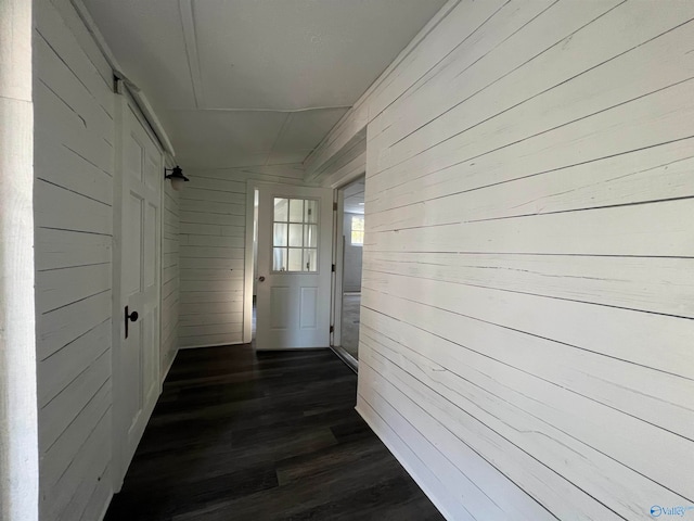 hallway with lofted ceiling, dark wood-type flooring, and wood walls