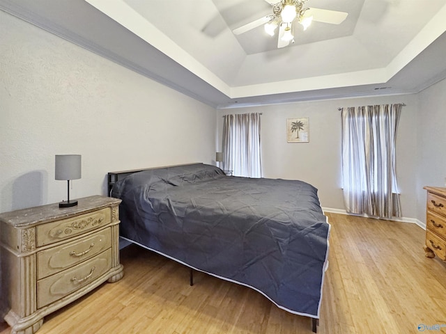 bedroom with ceiling fan, light hardwood / wood-style flooring, multiple windows, and a tray ceiling