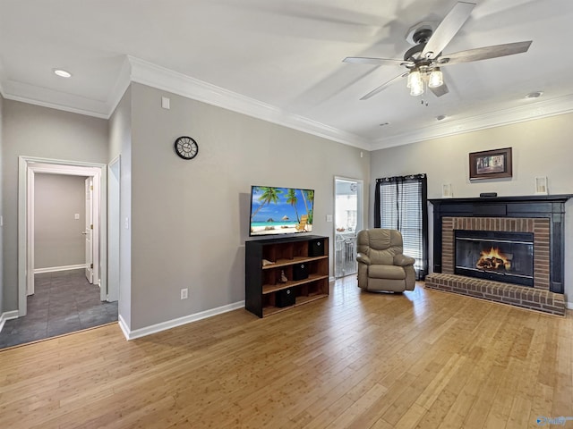 living room with wood-type flooring, a brick fireplace, ceiling fan, and crown molding