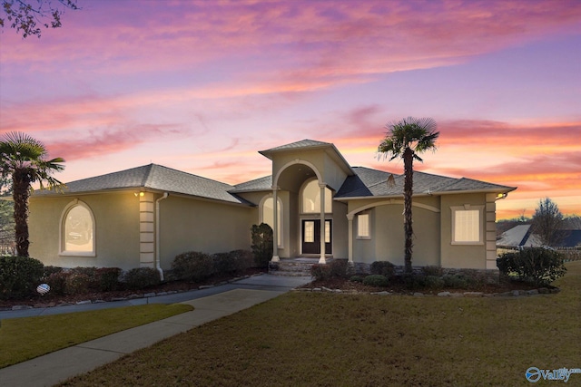 view of front facade with roof with shingles, a front yard, and stucco siding