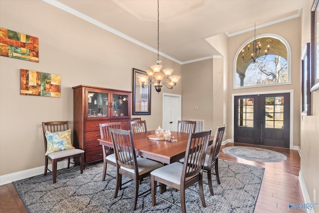 dining area with baseboards, wood finished floors, an inviting chandelier, crown molding, and french doors