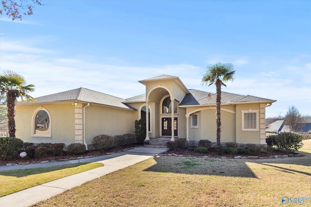 mediterranean / spanish home featuring a front lawn, roof with shingles, and stucco siding