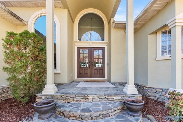 view of exterior entry featuring stone siding, french doors, and stucco siding