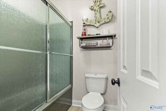 bathroom featuring toilet, baseboards, and a shower with shower door