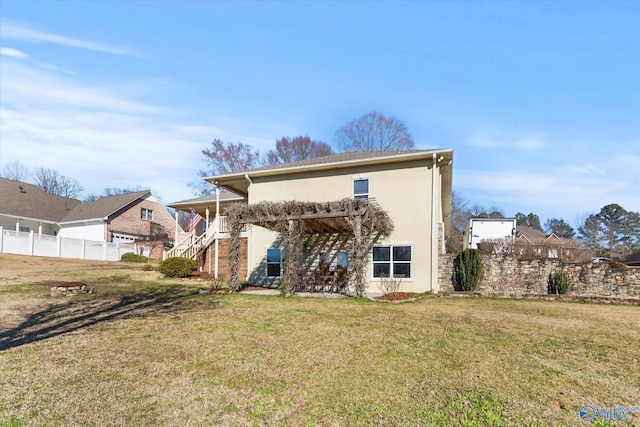 back of house with stairs, a lawn, fence, and stucco siding