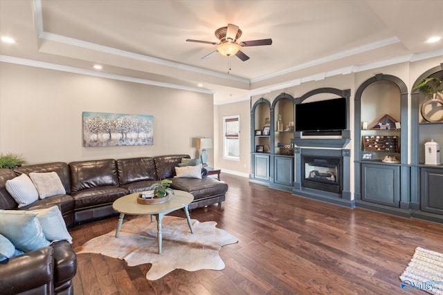 living area featuring ceiling fan, wood finished floors, a tray ceiling, crown molding, and a fireplace