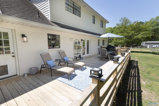 wooden deck featuring a trampoline, french doors, outdoor dining space, and a lawn