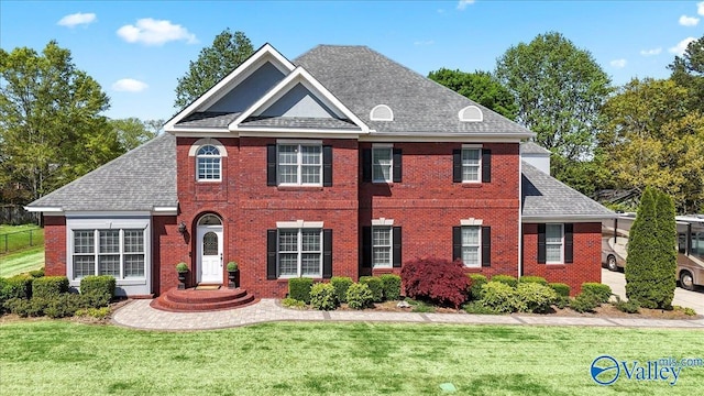 view of front of property featuring a front lawn, brick siding, and roof with shingles