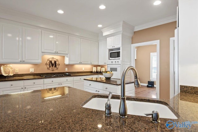 kitchen featuring dark stone counters, a sink, gas cooktop, oven, and white cabinets