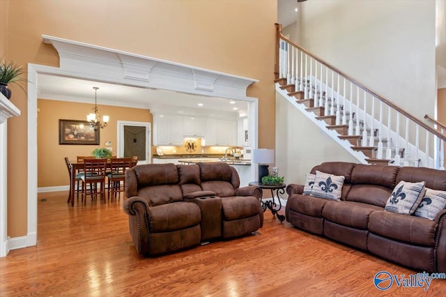 living room featuring an inviting chandelier, ornamental molding, a towering ceiling, and light wood-type flooring