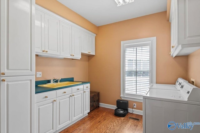 clothes washing area featuring a sink, light wood-style floors, washer and dryer, cabinet space, and baseboards