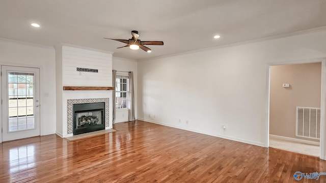 unfurnished living room with a fireplace, wood finished floors, visible vents, a ceiling fan, and ornamental molding