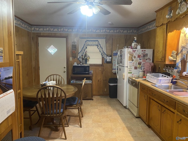 kitchen with sink, white appliances, a textured ceiling, and wood walls