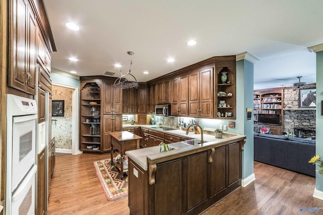 kitchen featuring black electric cooktop, kitchen peninsula, double oven, a fireplace, and light hardwood / wood-style floors