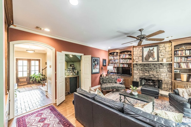 living room with a stone fireplace, ornamental molding, ceiling fan, and light wood-type flooring