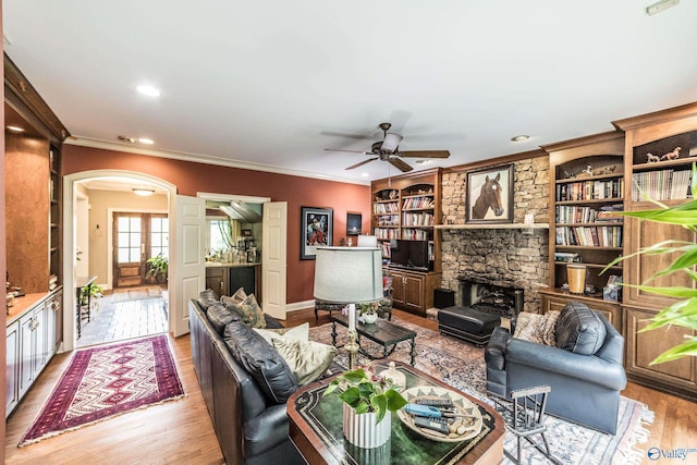 living room featuring crown molding, ceiling fan, a fireplace, and light wood-type flooring