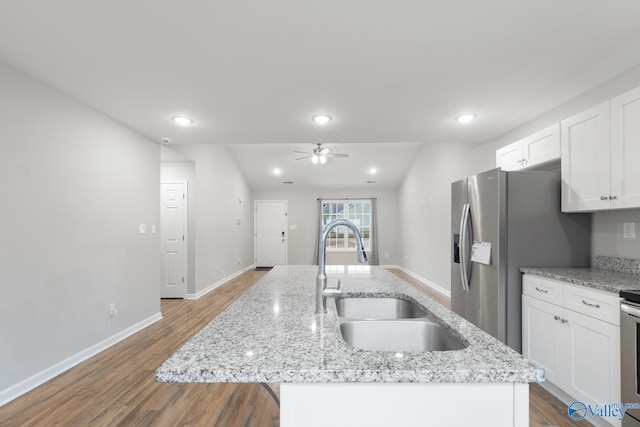 kitchen featuring stainless steel fridge, sink, white cabinets, light stone countertops, and an island with sink