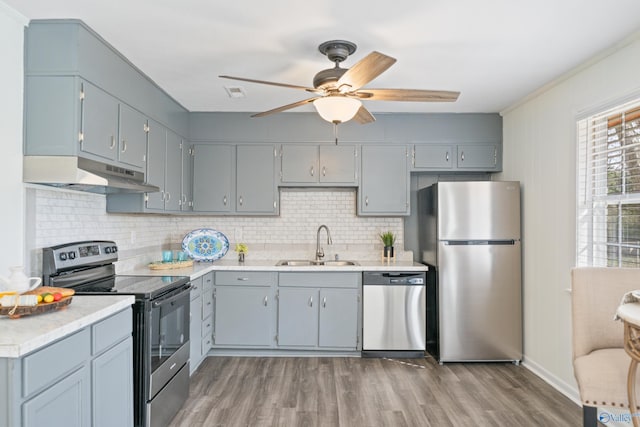 kitchen with light countertops, appliances with stainless steel finishes, a sink, wood finished floors, and under cabinet range hood