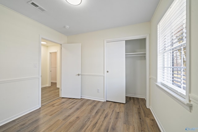 unfurnished bedroom with a closet, visible vents, baseboards, and wood finished floors