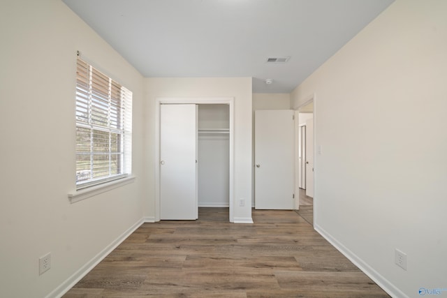 unfurnished bedroom with a closet, visible vents, baseboards, and wood finished floors