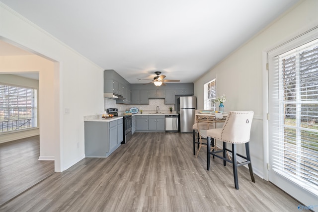 kitchen with light countertops, backsplash, gray cabinetry, appliances with stainless steel finishes, and a sink