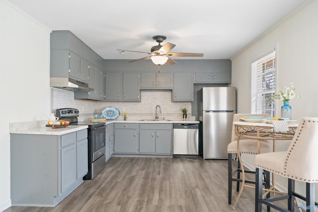 kitchen with under cabinet range hood, stainless steel appliances, a sink, light countertops, and gray cabinets