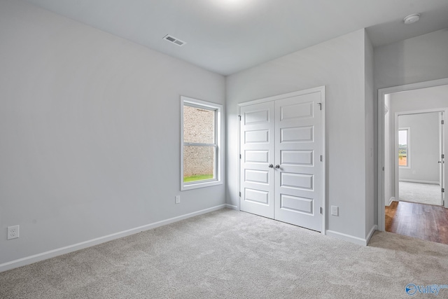 unfurnished bedroom with light carpet, multiple windows, visible vents, and baseboards