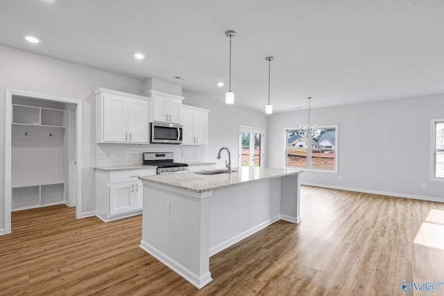 kitchen featuring decorative light fixtures, appliances with stainless steel finishes, a kitchen island with sink, white cabinets, and a sink