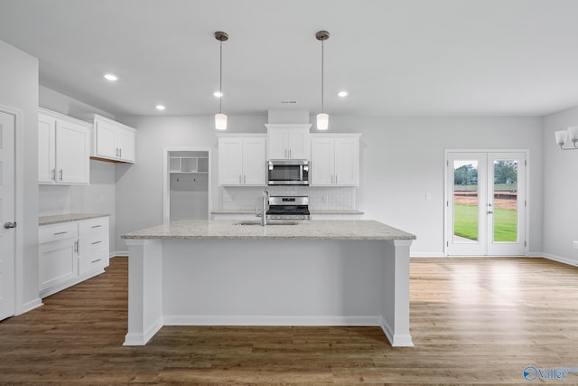 kitchen with stainless steel appliances, white cabinets, hanging light fixtures, and light stone counters