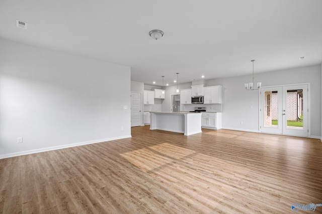 unfurnished living room with an inviting chandelier, light wood-style flooring, visible vents, and baseboards