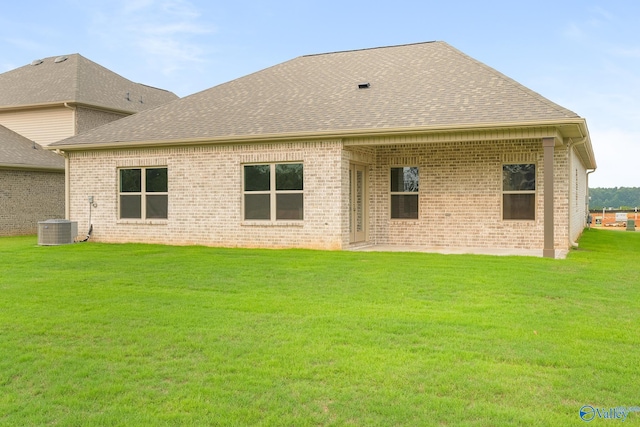 rear view of house with central AC, brick siding, roof with shingles, and a lawn