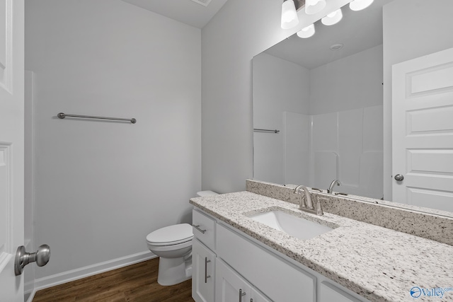 bathroom featuring baseboards, toilet, wood finished floors, walk in shower, and vanity