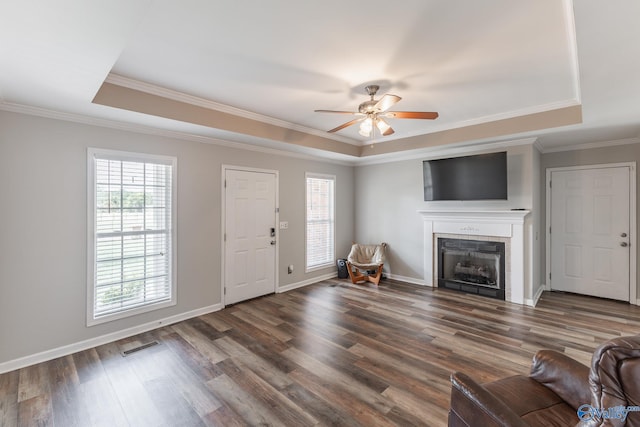 unfurnished living room featuring hardwood / wood-style floors, a tray ceiling, a fireplace, and ceiling fan