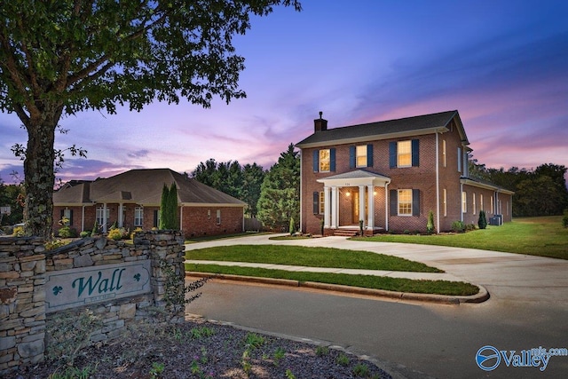 view of front of house with brick siding, a lawn, and a chimney