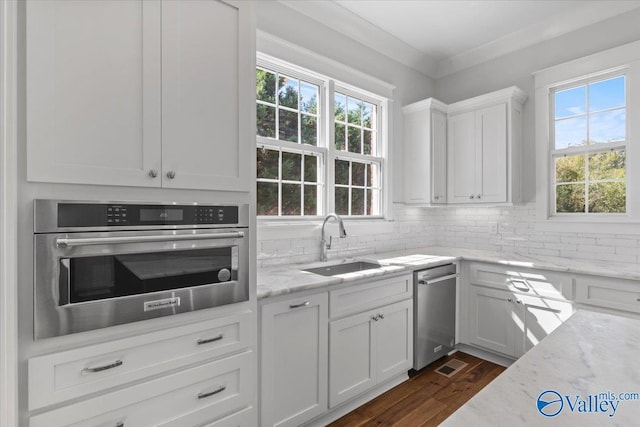 kitchen featuring crown molding, backsplash, white cabinetry, stainless steel oven, and a sink