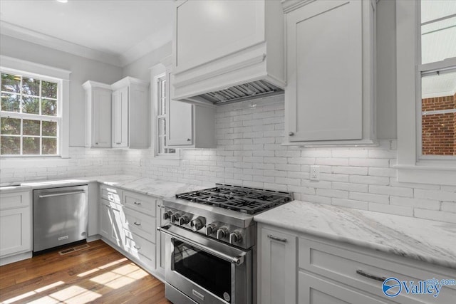 kitchen with tasteful backsplash, appliances with stainless steel finishes, crown molding, premium range hood, and white cabinetry