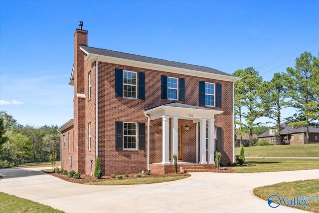 view of front of house featuring brick siding, driveway, a chimney, and a front lawn